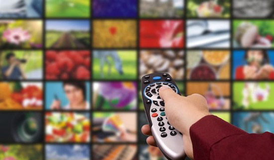 Hand and TV remote pointed at wall of television screens