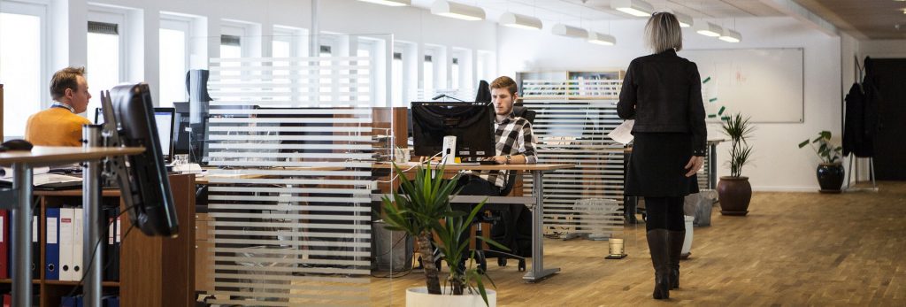 Open plan office with people at desks and woman walking away