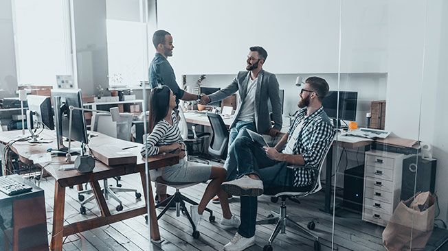 Relaxed business meeting with four people in an office, two of them shaking hands