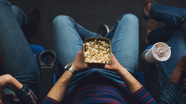 Overhead shot of man sitting in cinema chair with popcorn in lap and drink in cup-holder